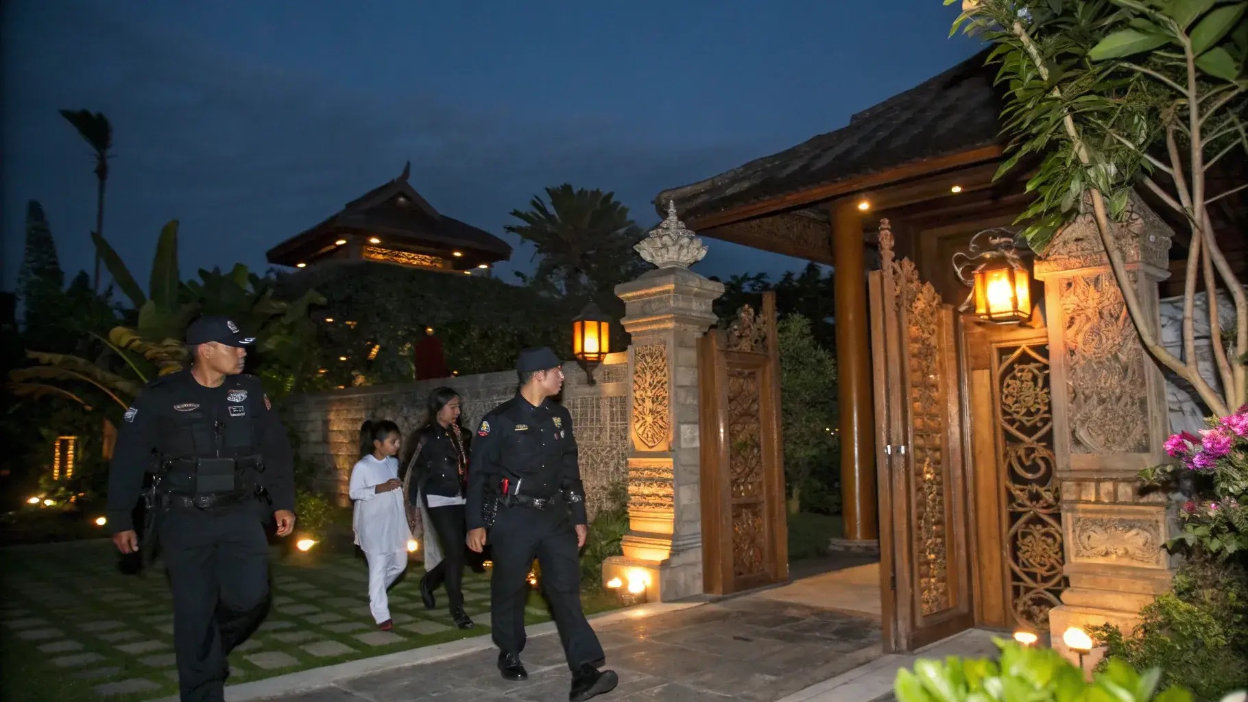 Security officers escorting a family through the gate of a Balinese villa at dusk